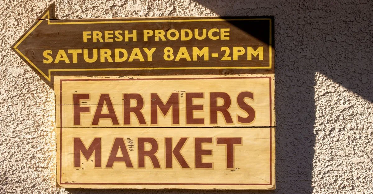 A hand-painted wooden sign pointing toward a Saturday morning farmers market