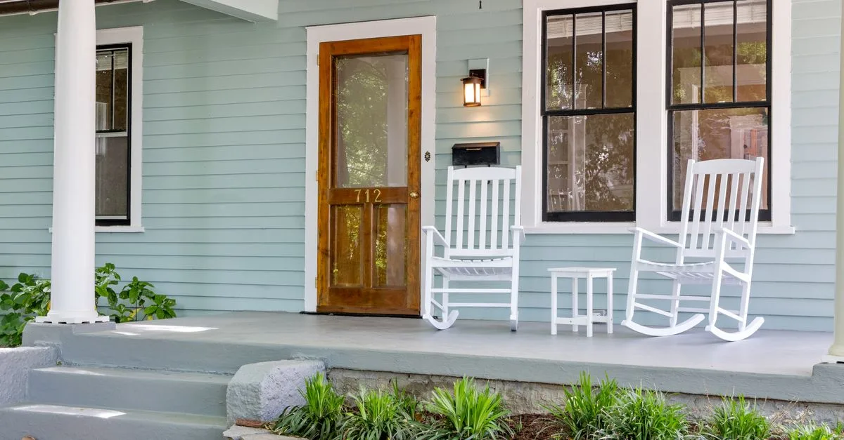 A pale green Craftsman bungalow porch with two white rocking chairs.