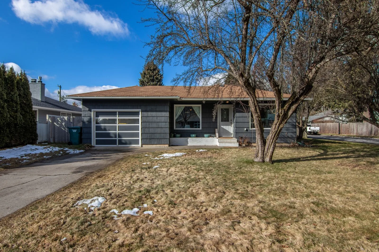 Single-story 1960s ranch home with a mature tree on a quiet street