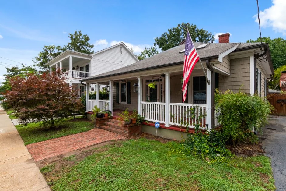 A cottage-style bungalow with a porch flag on a residential street