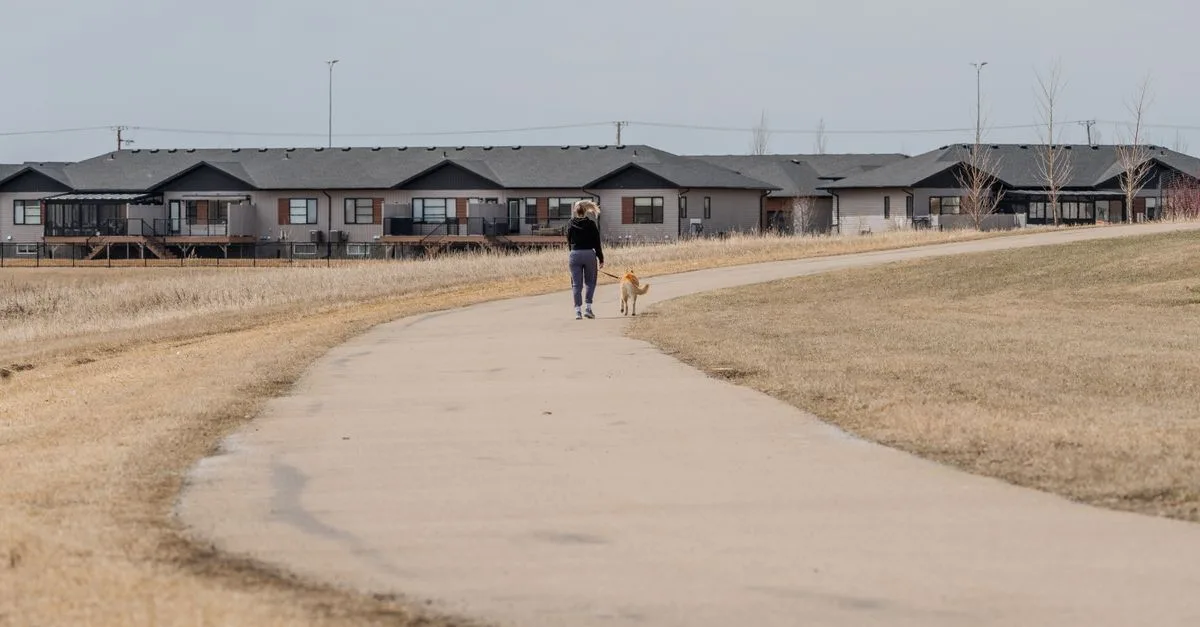 Dog walker on a paved path past ranch-style townhomes