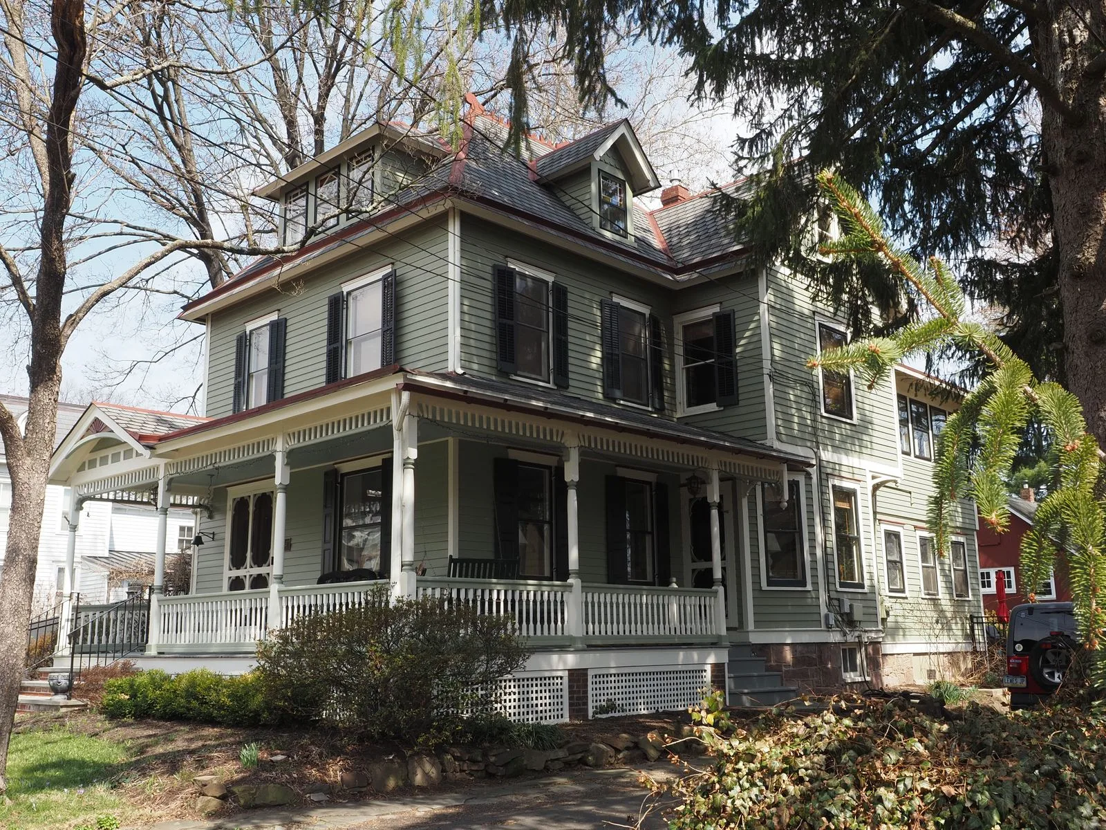 A Victorian house with a wraparound porch on a tree-shaded street