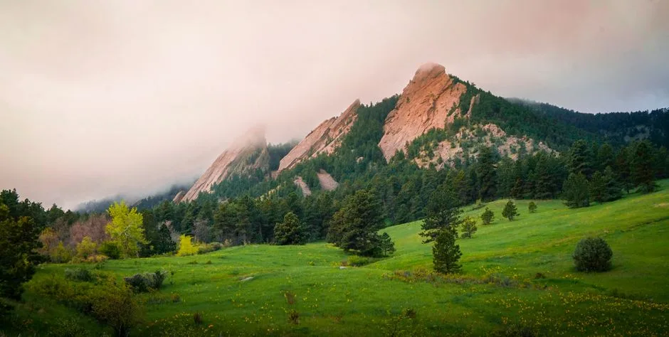 Fog drifts over rocky foothills and a green meadow in the Front Range near Boulder