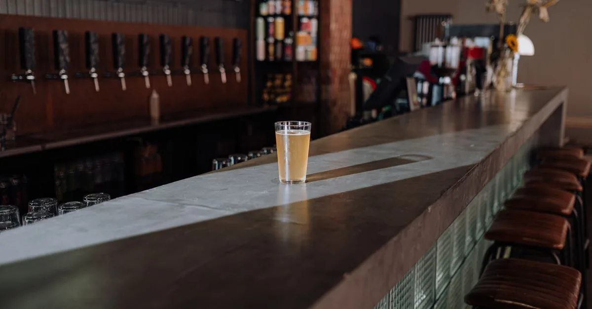 A pint of beer on a concrete bar top with taps lined up behind it at a brewery taproom