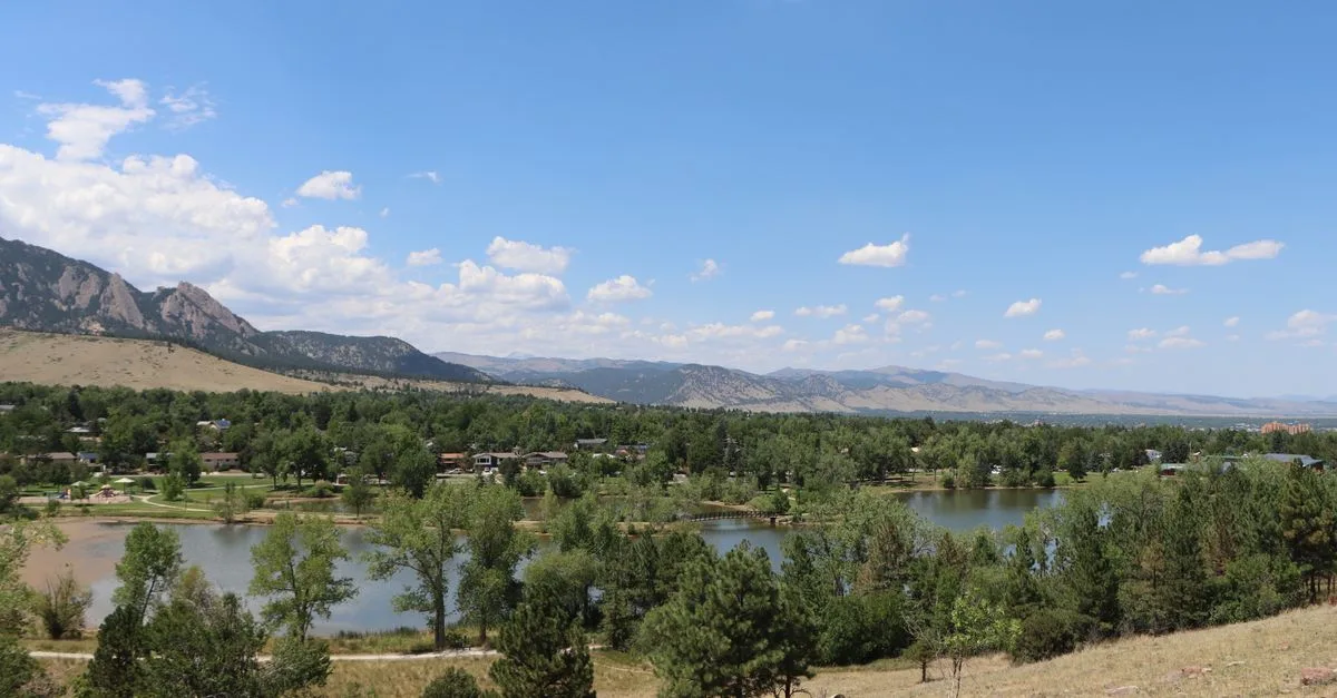 Flatirons foothills rise behind a lake and tree-lined neighborhood in Boulder, Colorado