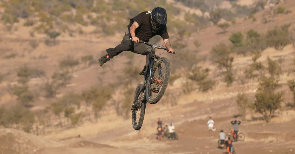 Mountain biker catching air off a dirt jump on a scrubby hillside track