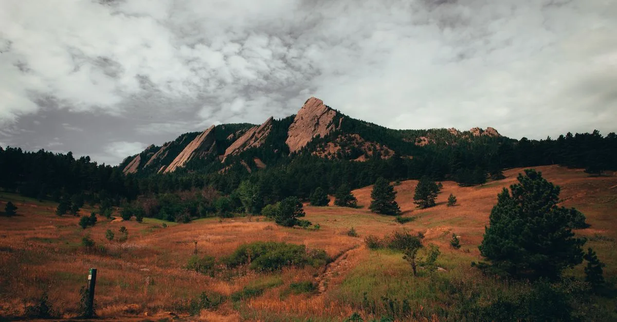 A dramatic view of the Flatirons rock formations above a golden meadow trail