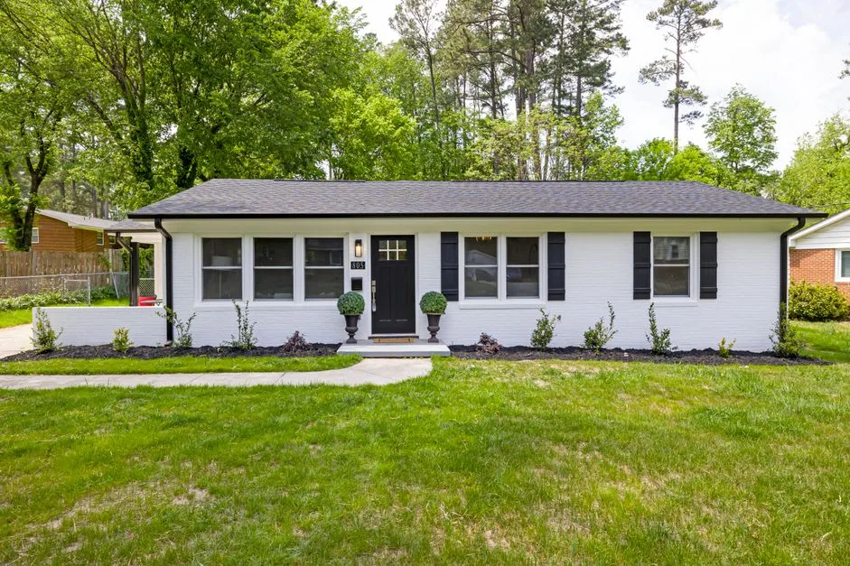White one-story ranch home with a lawn and shade trees