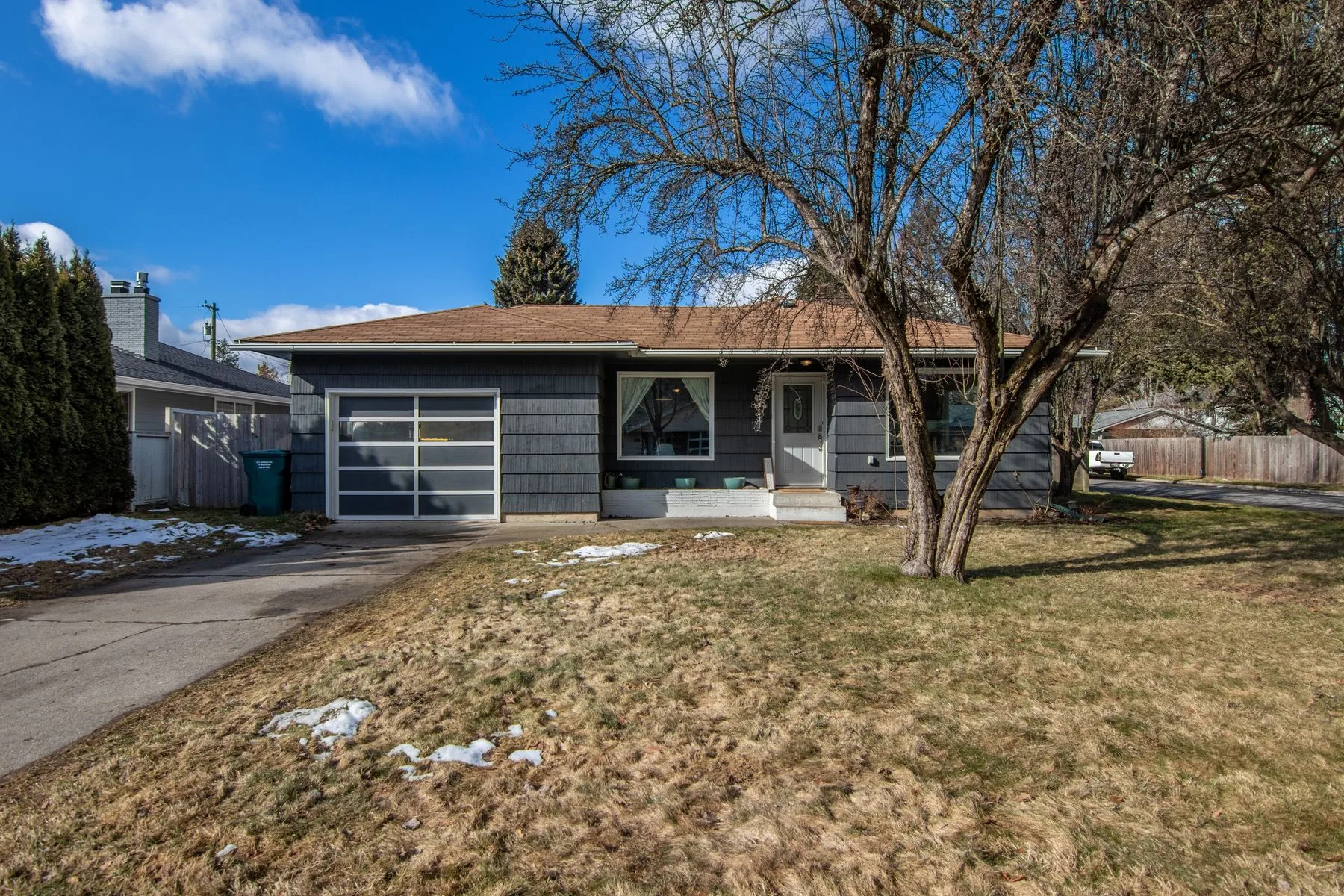 Single-story ranch home with a bare tree and patchy snow on the lawn