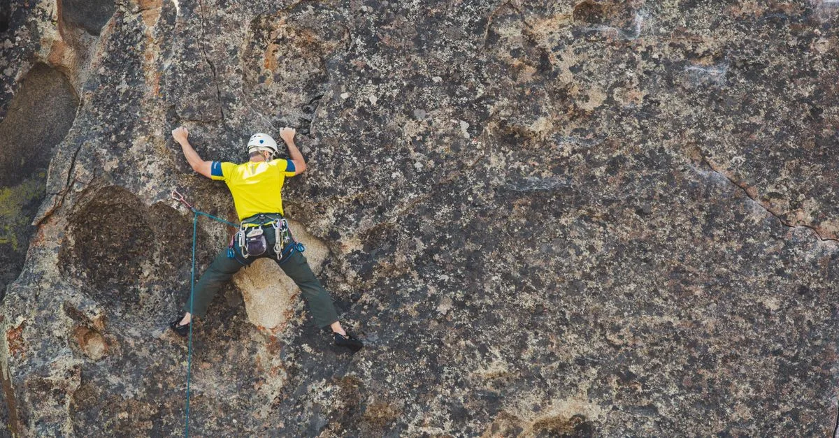 A rock climber scaling a lichen-covered granite cliff face