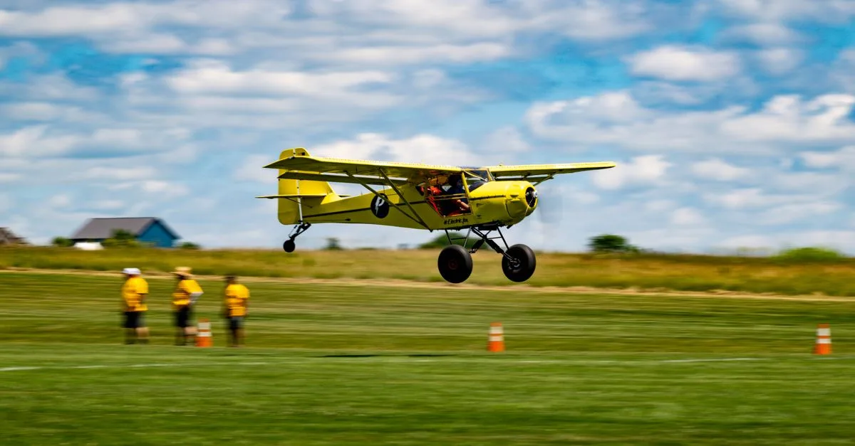 A small yellow plane landing on a grass runway at a rural airfield