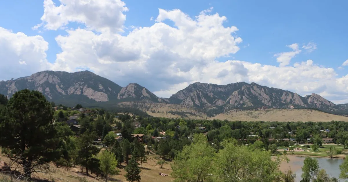 The Flatirons rise above a tree-lined Boulder neighborhood and lake