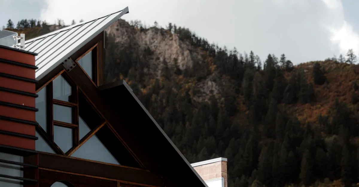 A modern home's angled metal roofline against a forested foothill